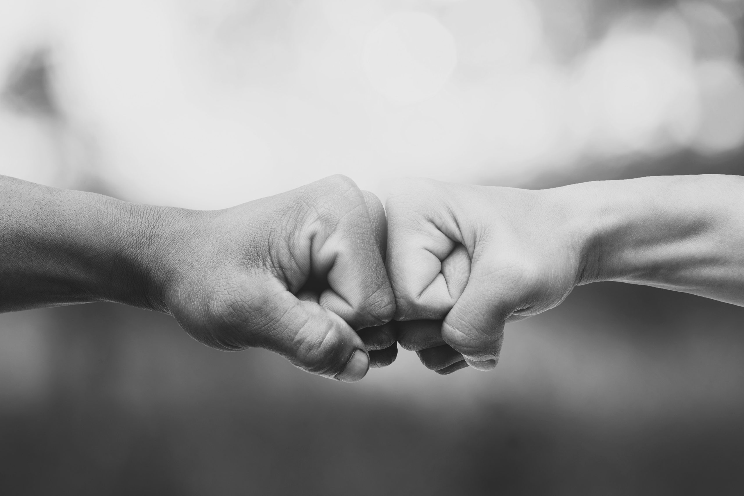 Ein Fistbump mit seitlicher Sicht auf Hände. Bild in schwarz-weiß.